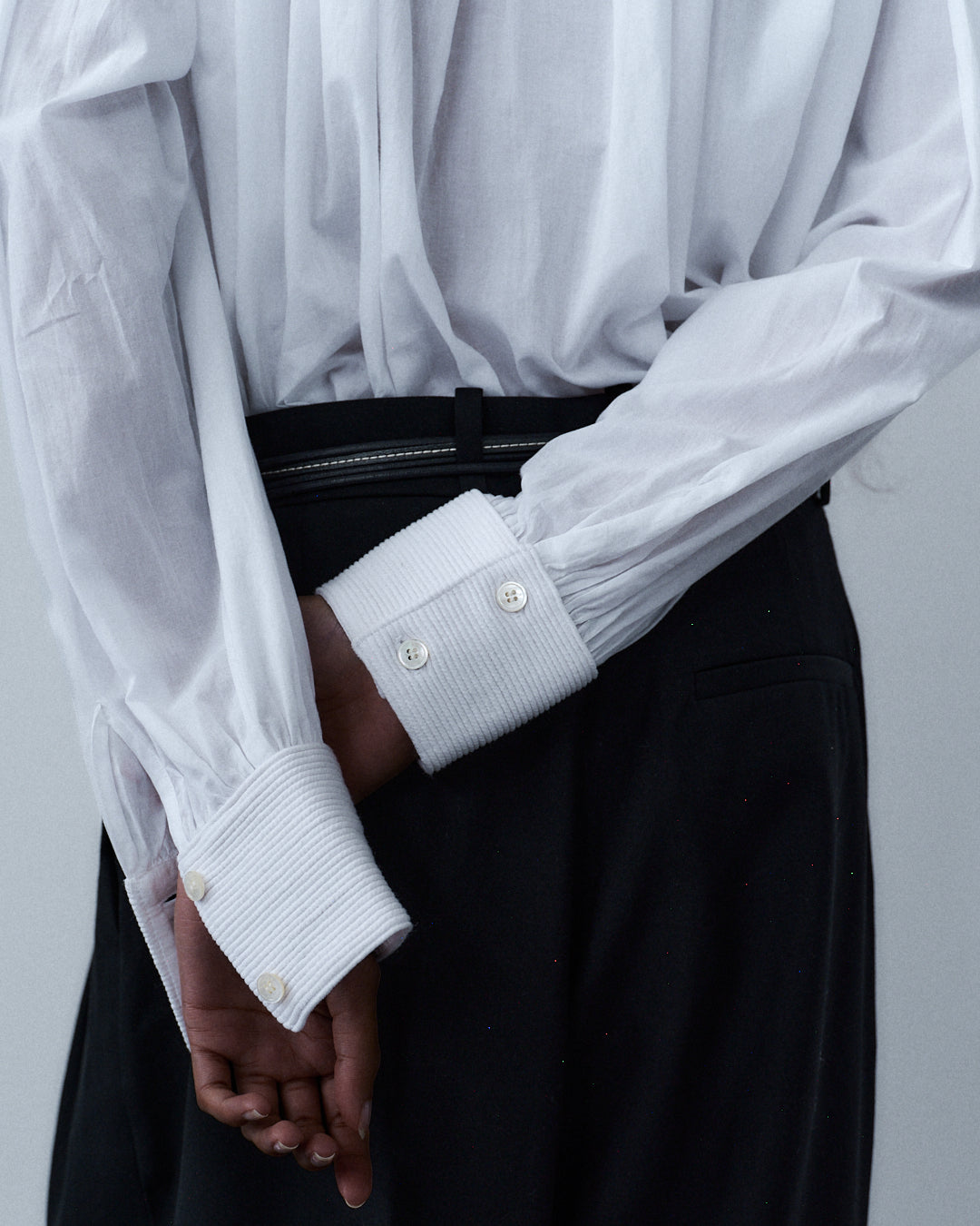 White sculptural shirt with ribbed cuffs and mother of pearl buttons, paired with black trousers