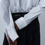 White sculptural shirt with ribbed cuffs and mother of pearl buttons, paired with black trousers