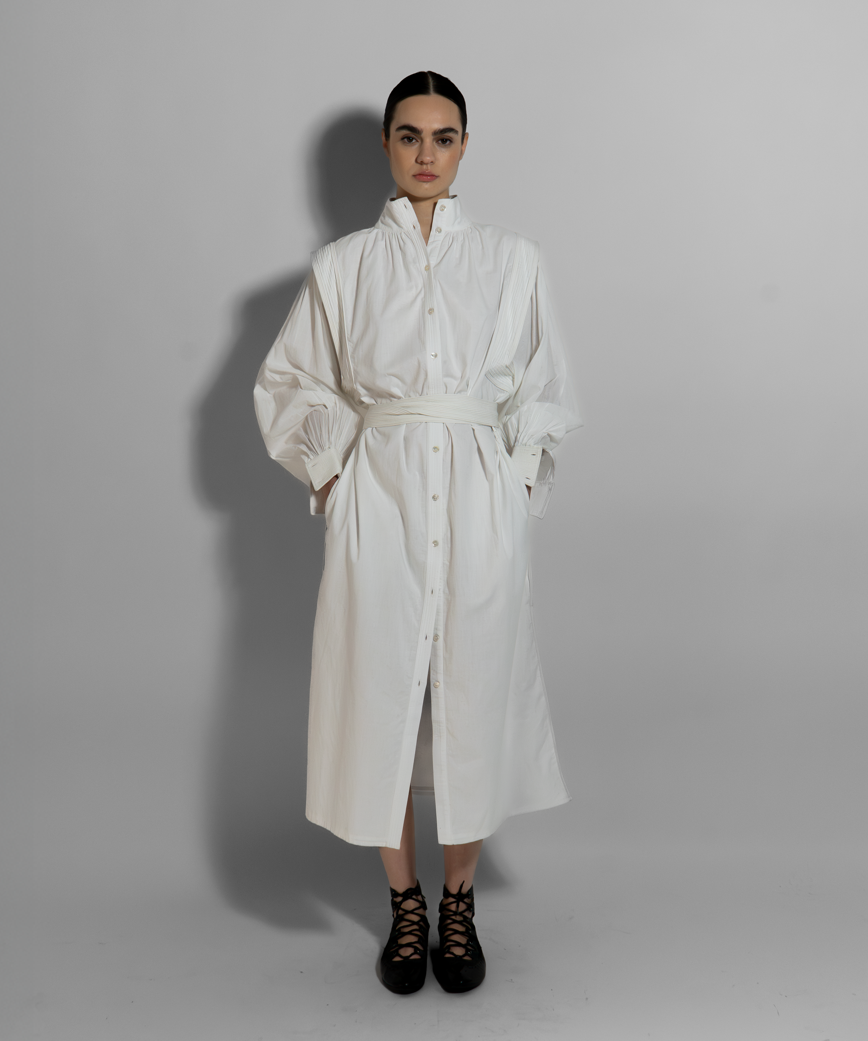 Woman wearing MAY white cotton voile dress with hand-embroidered cuffs, belted silhouette, paired with black lace-up boots on neutral background