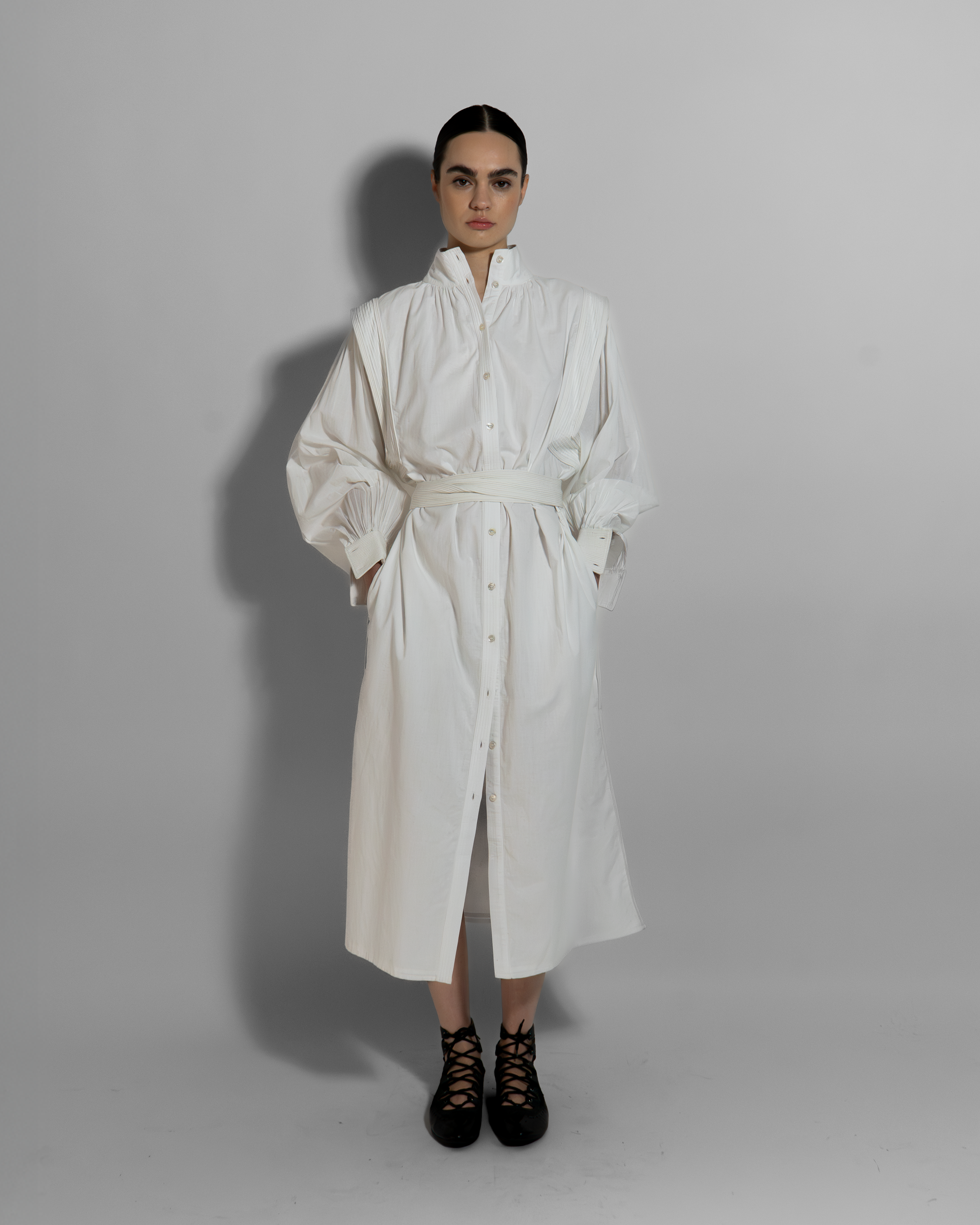 Woman wearing MAY white cotton voile dress with hand-embroidered cuffs, belted silhouette, paired with black lace-up boots on neutral background