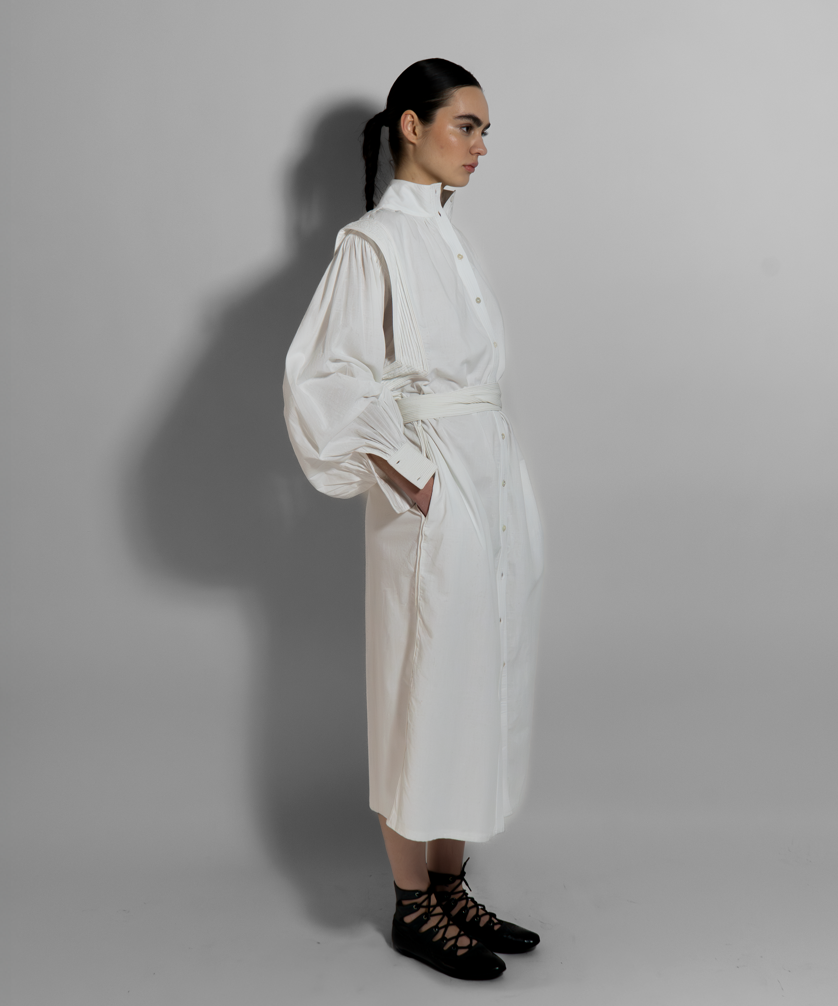 Woman wearing white cotton voile MAY dress with hand-embroidered cuffs, paired with black lace-up boots, embodying minimalist luxury