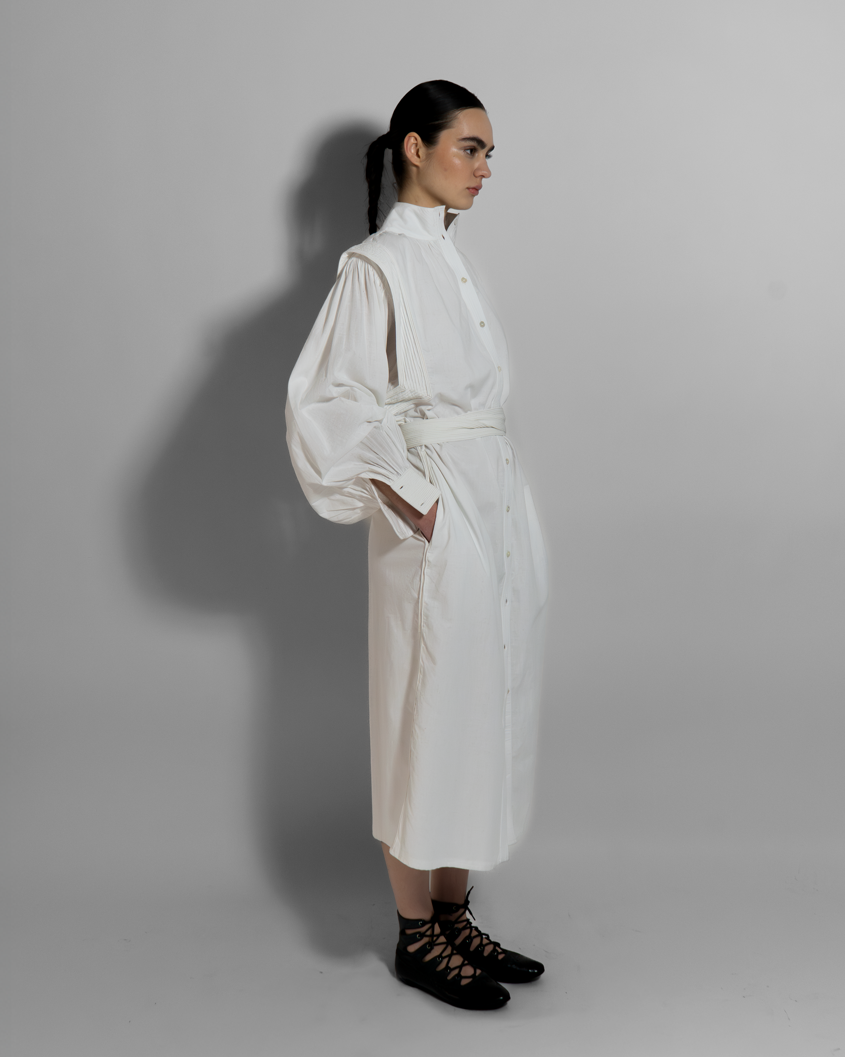 Woman wearing white cotton voile MAY dress with hand-embroidered cuffs, paired with black lace-up boots, embodying minimalist luxury