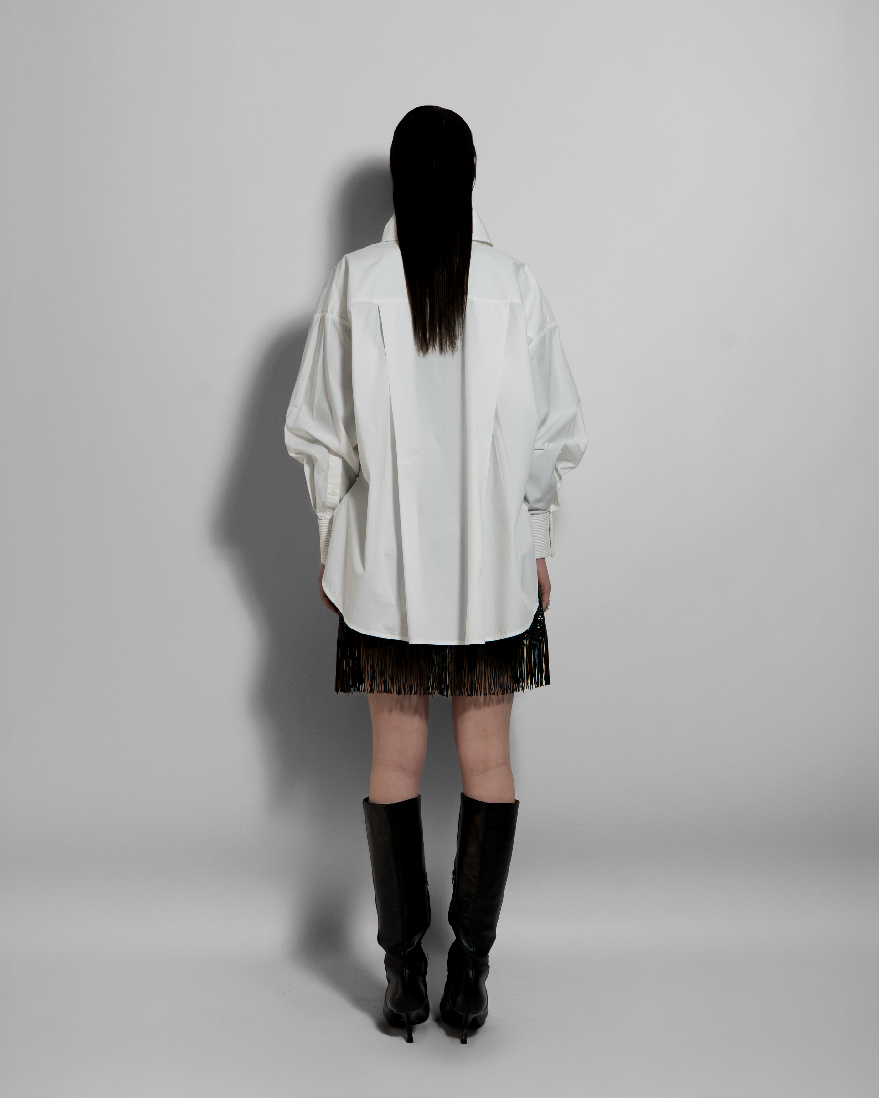 ELE white cotton poplin shirt with hand-embroidered details, oversized voluminous cut, rear view on model with black fringed skirt
