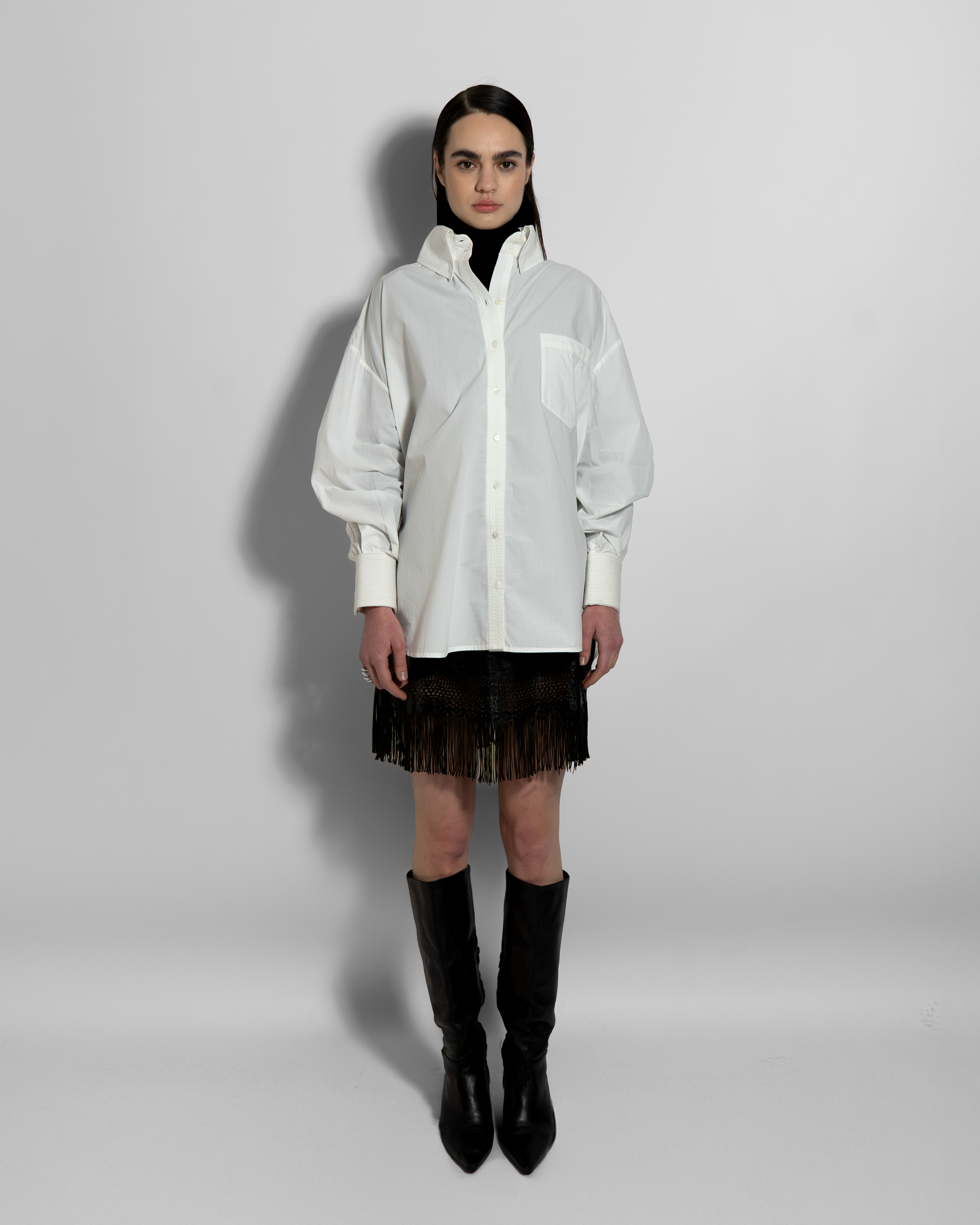 White cotton poplin ELE shirt with voluminous oversized cut and hand-embroidered details, styled with black fringe skirt and boots