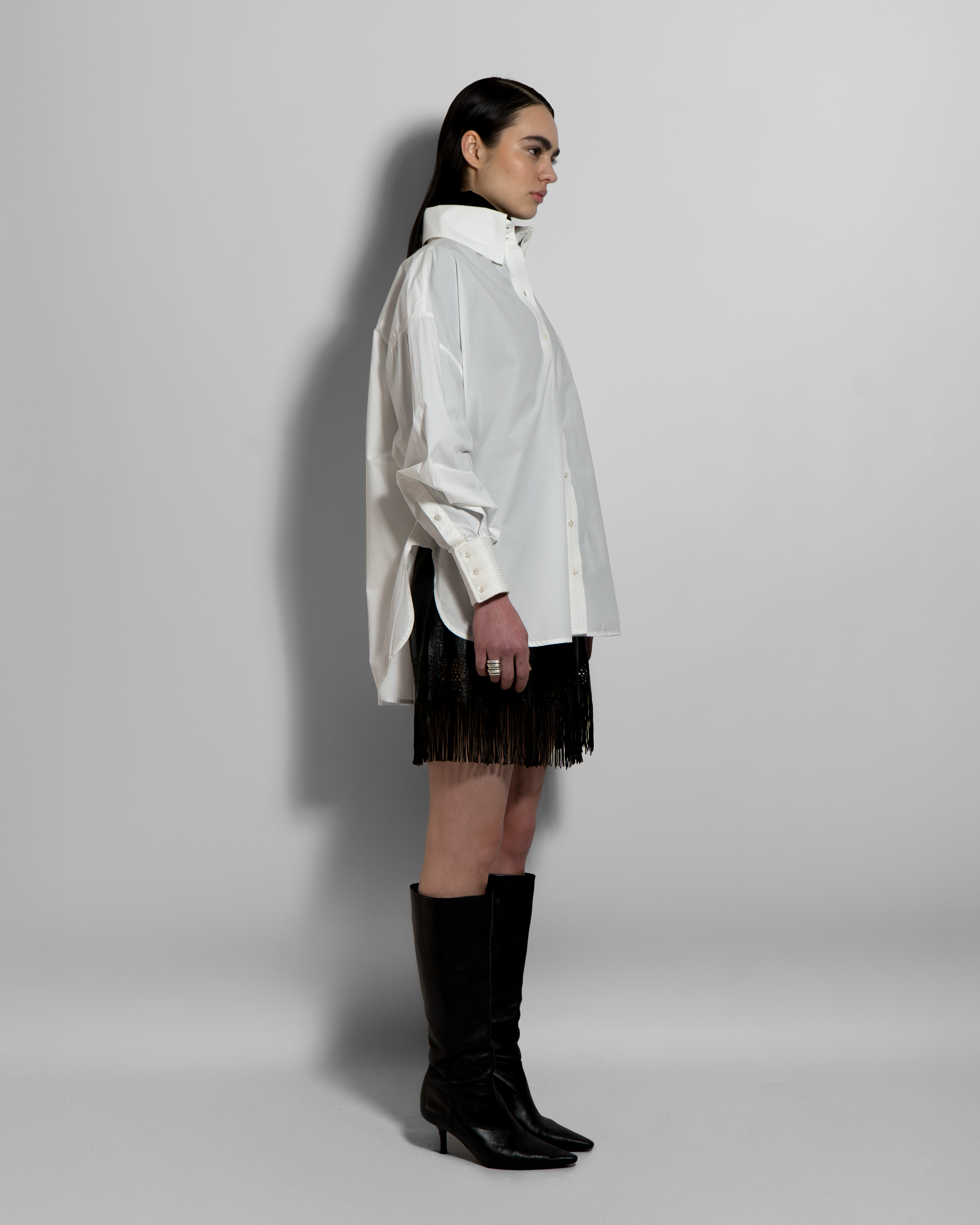 White cotton poplin ELE shirt with hand-embroidered details, oversized cut, worn with black fringe skirt and boots